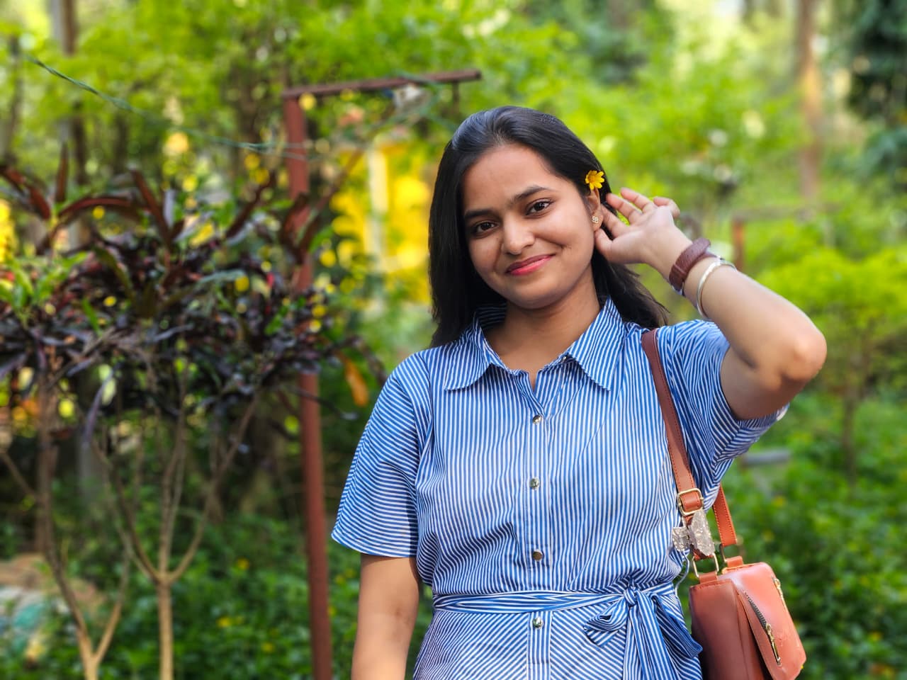 Subhasree wearing a blue striped dress with a yellow flower, in a green garden